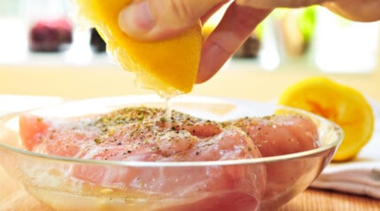A piece of chicken breast being prepared to marinate in herbs and lemon juice.