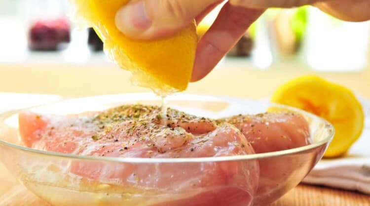 A piece of chicken breast being prepared to marinate in herbs and lemon juice.