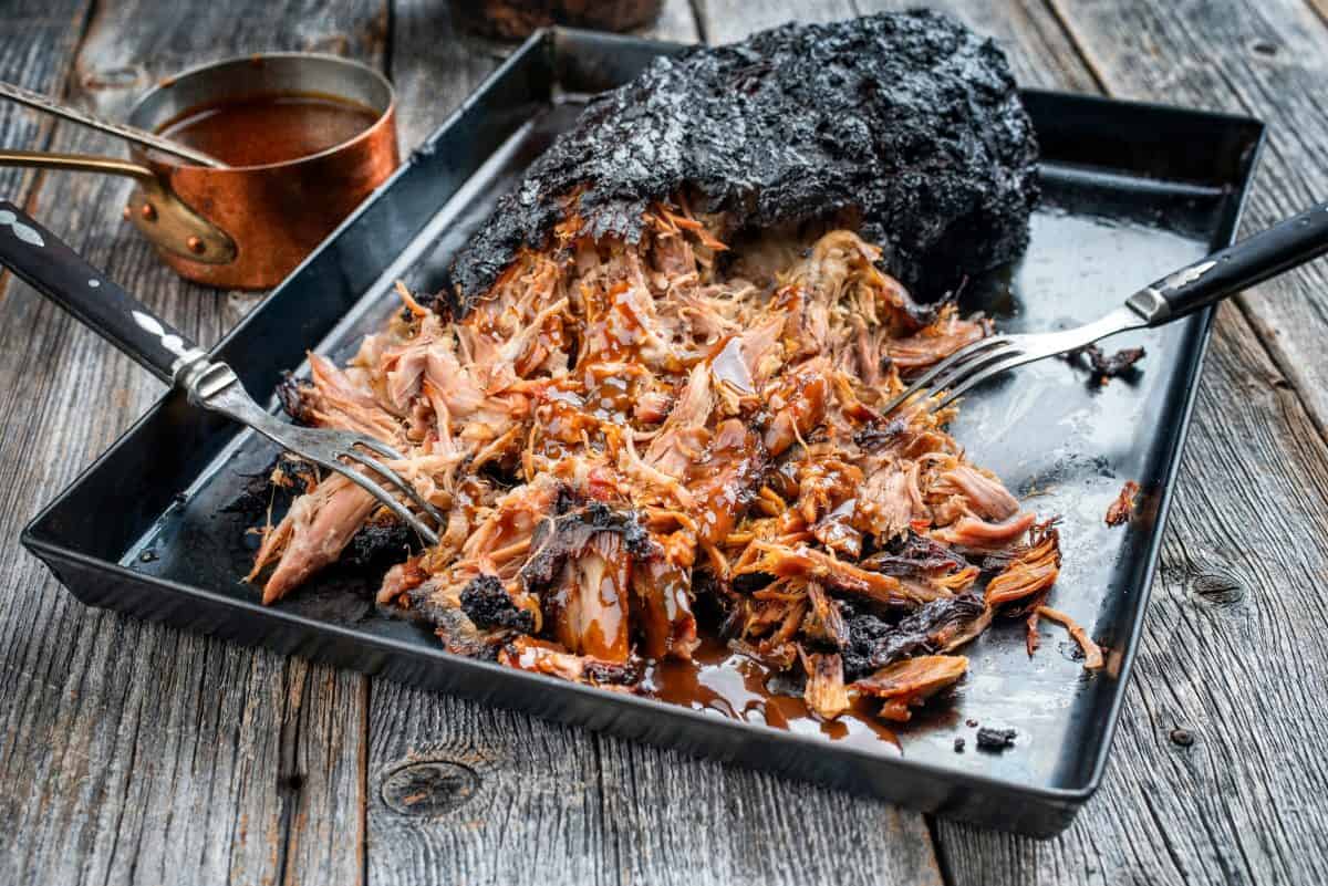 Pulled pork with a dark bark crust, on a shallow baking tray