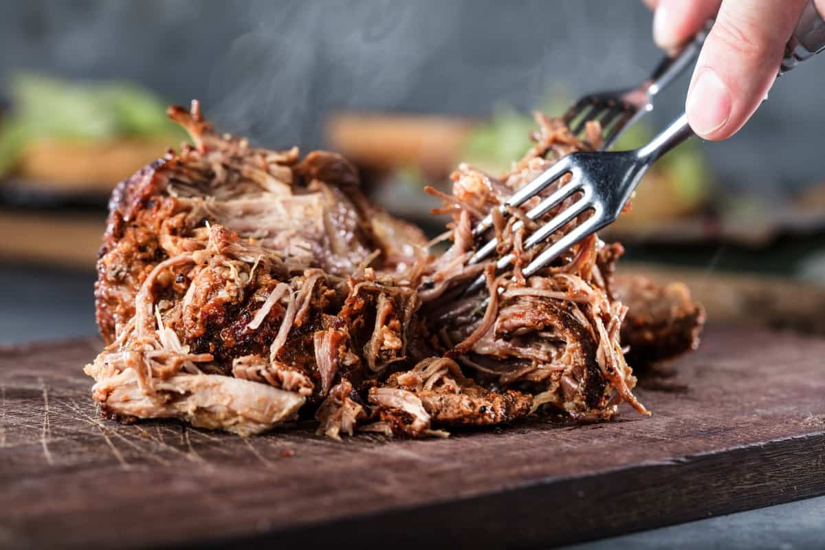 Pulled pork on a cutting board being pulled apart with fo.
