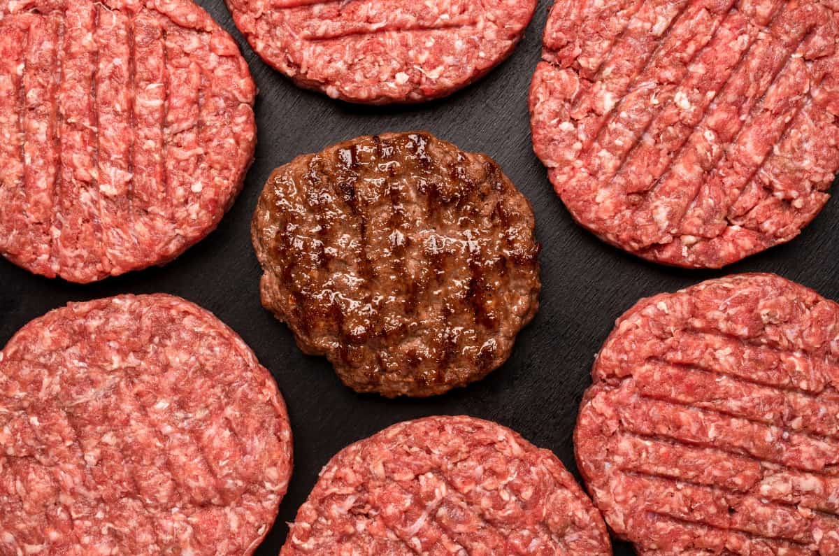 A cooked burger surrounded by raw burgers shot from above