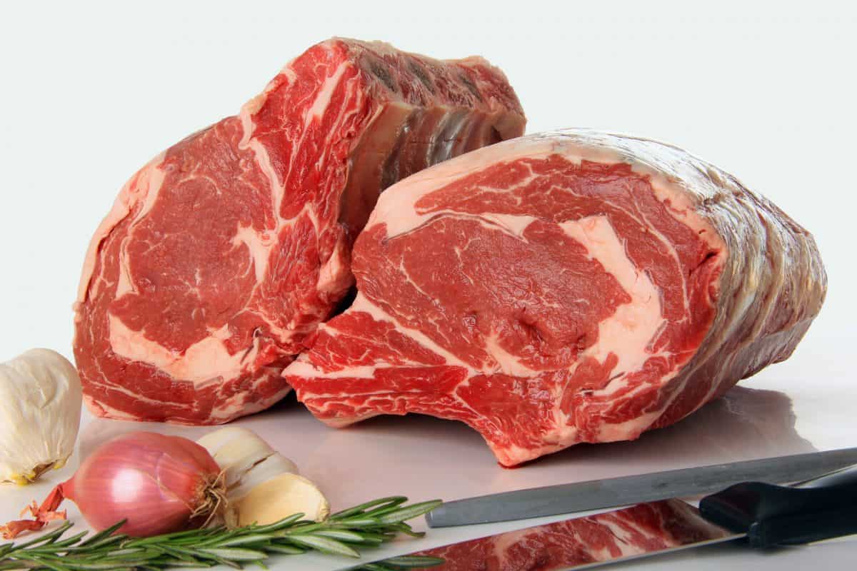 Side view of two uncooked prime rib roasts with some onion and herbs