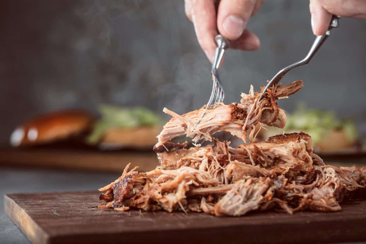 reheated pulled pork being shredded with forks on a cutting bo.
