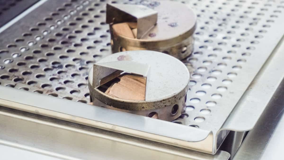 Two circular smoker boxes of wood chips on a grill