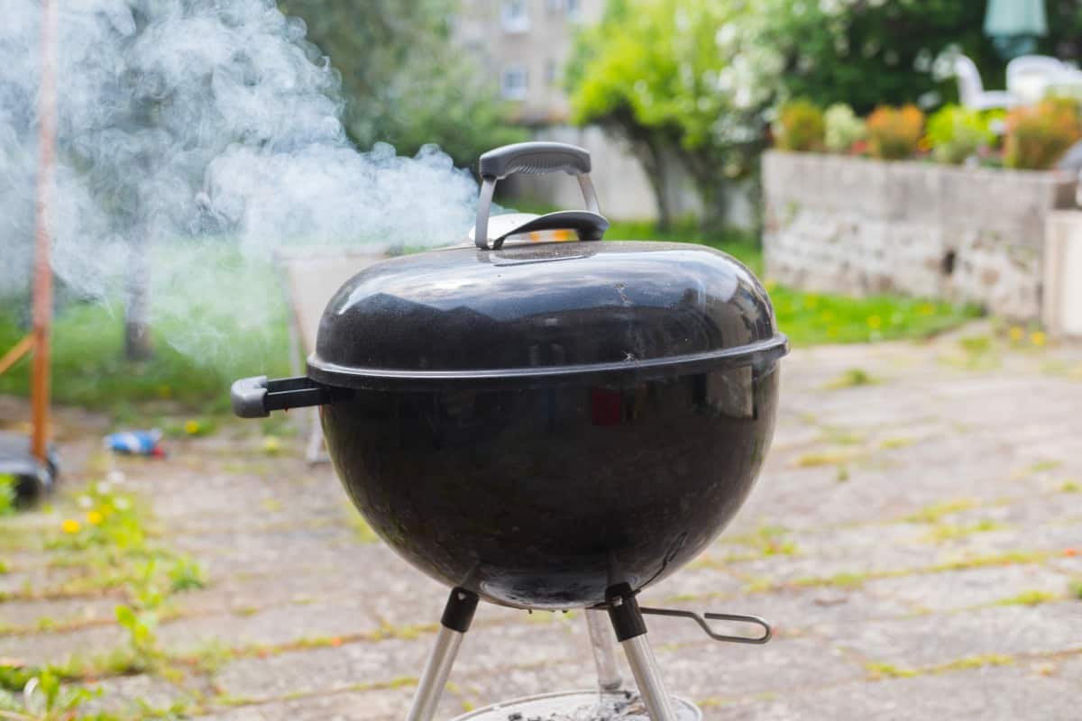 A smoking charcoal kettle grill on a patio