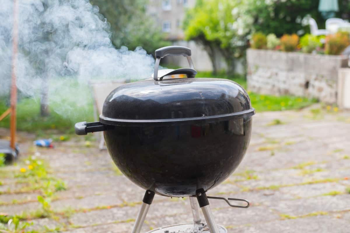 A smoking charcoal kettle grill on a pa.