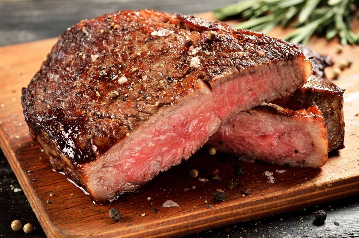 Close up of a grilled steak sliced in half, with blurred rosemary in background