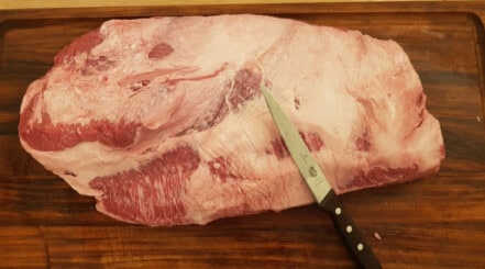 A whole wagyu brisket being trimmed on a chopping board.