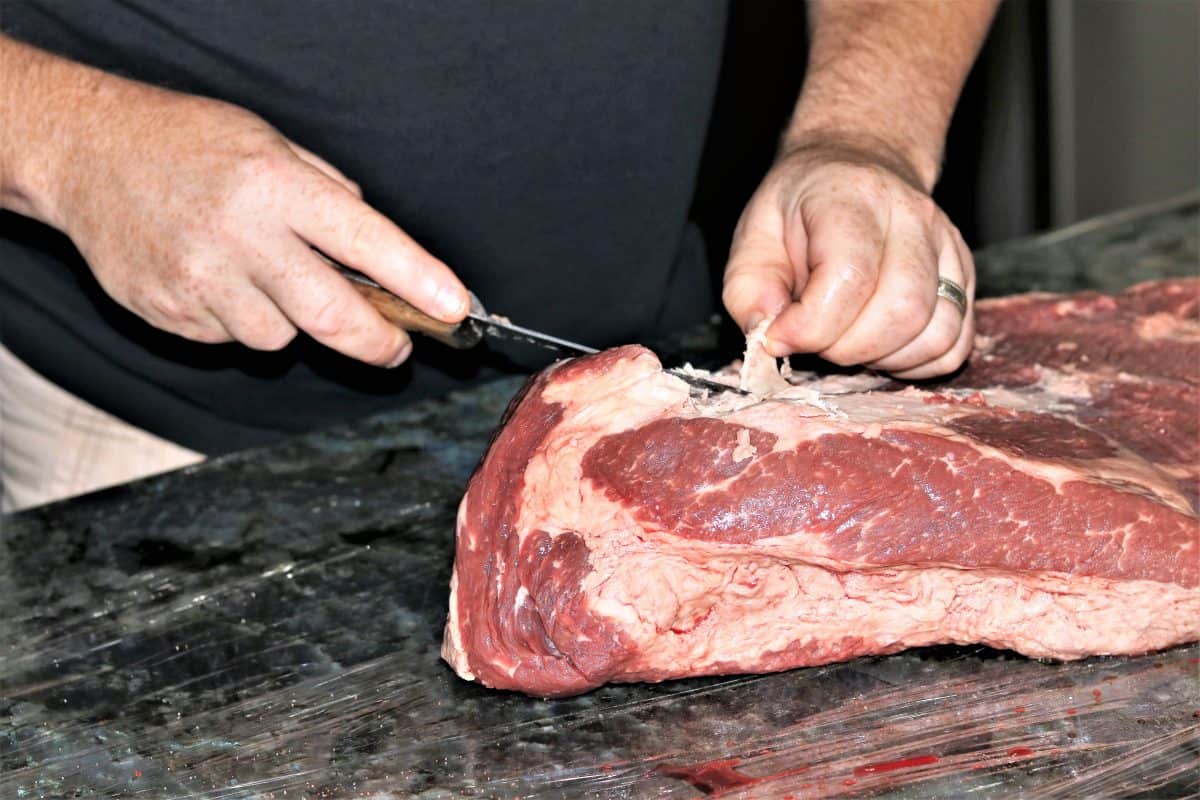 A man with a small knife trimming a brisket