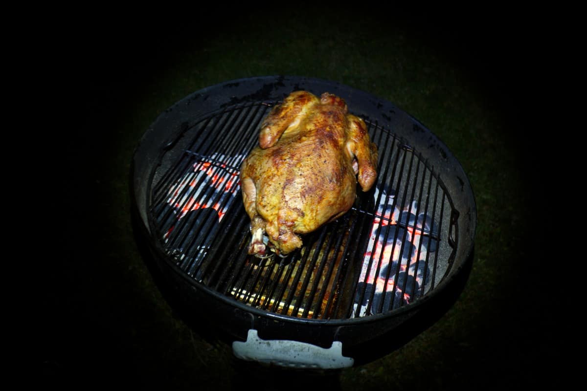 A turkey grilling indirect on a charcoal grill in the d.
