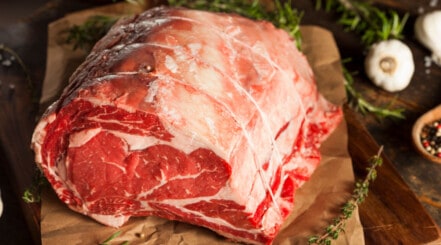 Prime rib on a chopping board with a few sprigs of fresh rosemary.