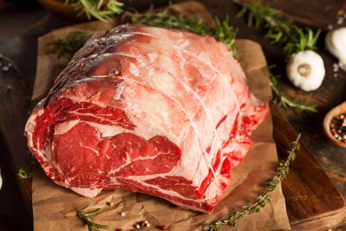 Prime rib on a chopping board with a few sprigs of fresh rosemary