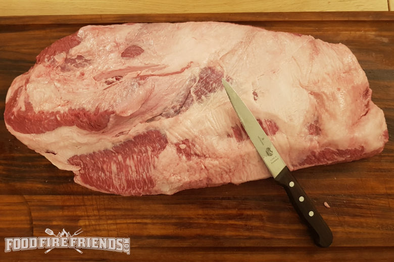 A whole wagyu brisket being trimmed on a chopping board