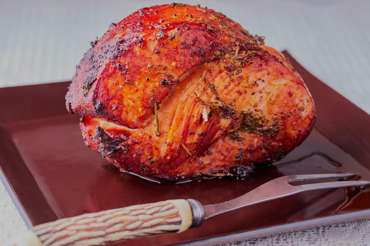 A large gammon joint being rested on a cutting board, next to a two prong f.