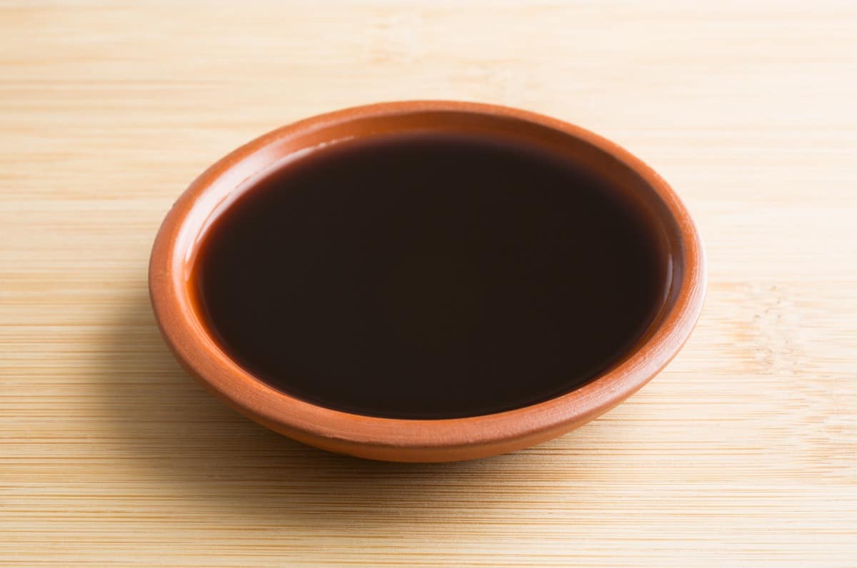 A brown bowl of liquid smoke on a light wood surf.