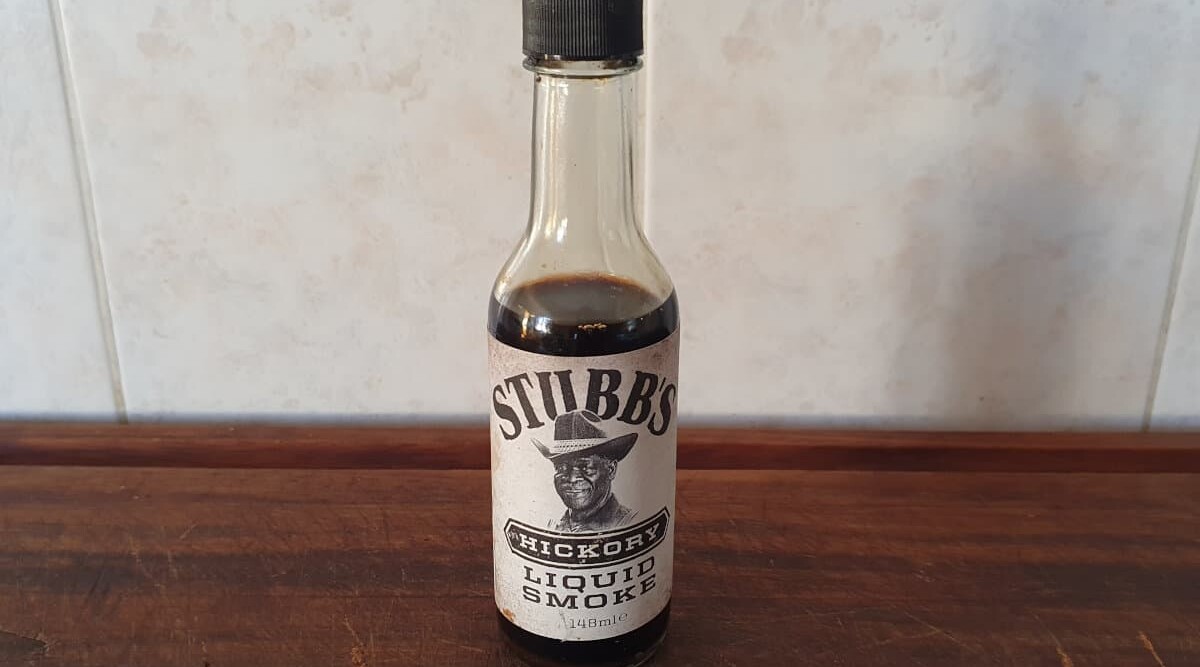 A bottle of Stubbs liquid smoke on a wooden cutting board.