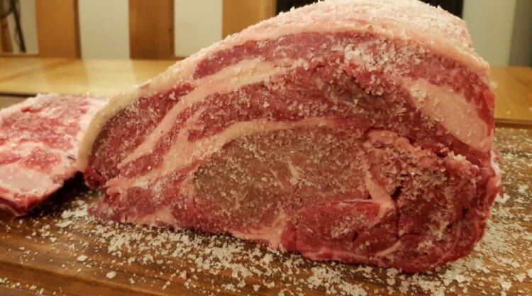 Close up of a dry brining prime beef rib with ribs removed, sitting on a chopping board