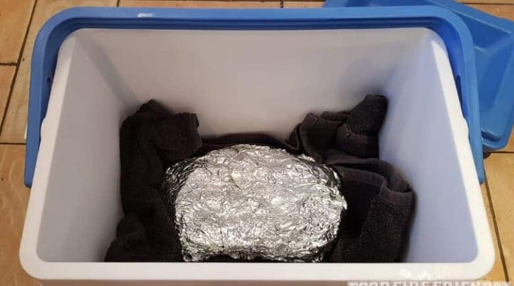 Meat, wrapepd in foil, in a blue cooler, with towels underneath