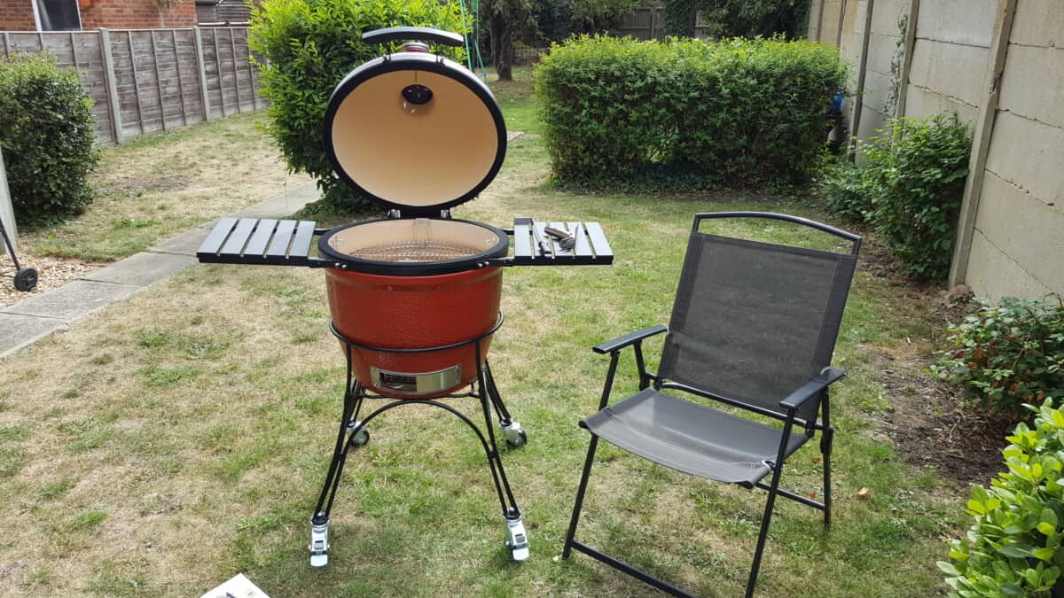 Kamado Joe classic v1 on a grass lawn with lid open, next to a black garden chair.