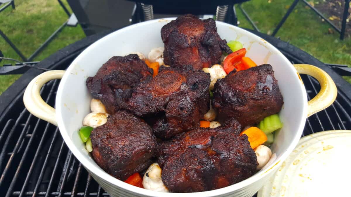 Smoked ox tails in a white dish with vegetables underneath.