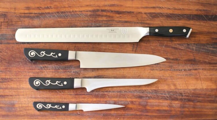 close up shot of a chefs, a paring, a boning and a slicing knife on a wooden chopping board