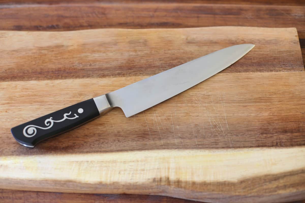 A Japanese style chefs knife on a wooden cutting bo.