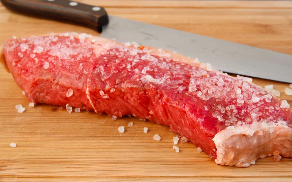 A beef steak coated liberally with coarse salt to dry brine it