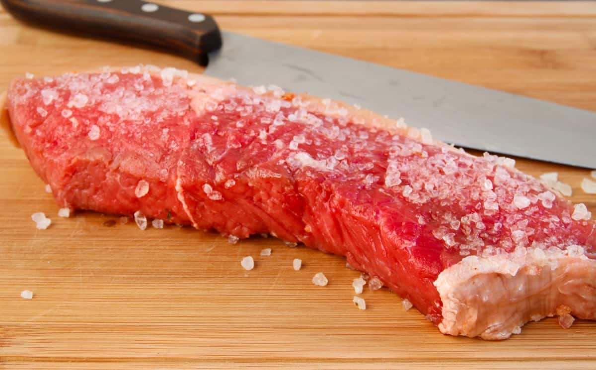 A beef steak coated liberally with coarse salt to dry brine.