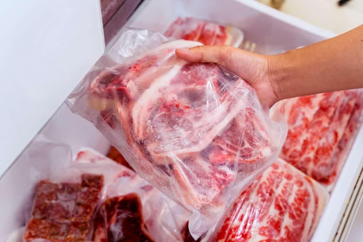 A hand placing a bag of meat into a freezer drawer