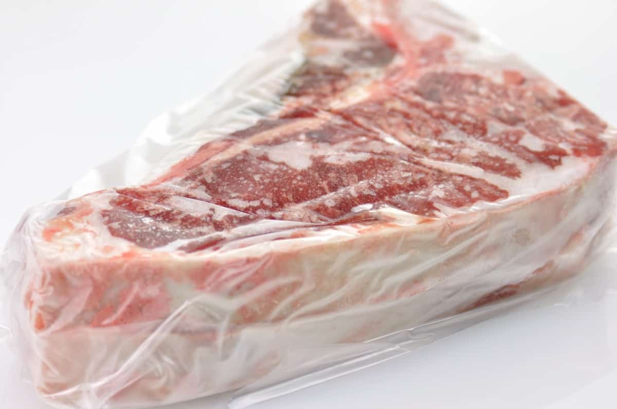 frozen t-bone steak in a freezer bag, isolated on wh.