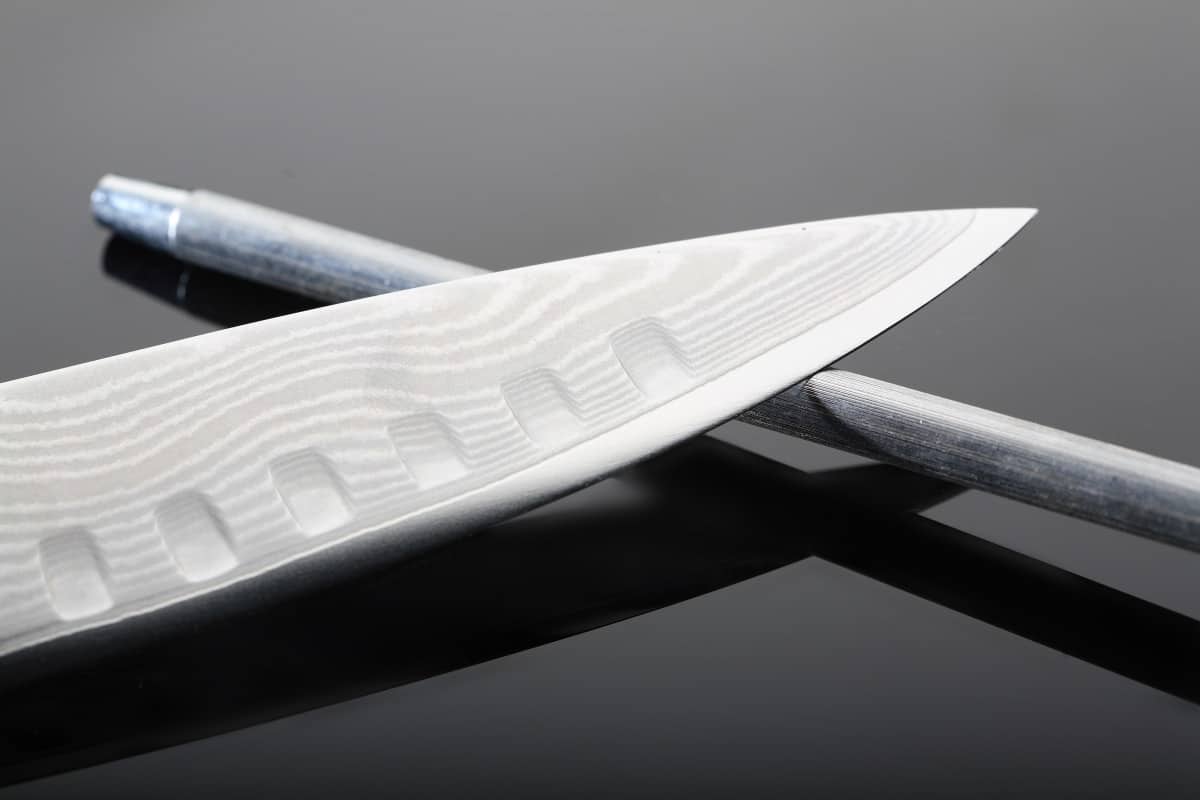 A knife resting on honing steel, on a shiny black background