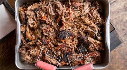 Smoked pulled pork in a metal serving tray with a pair of meat shredding claws