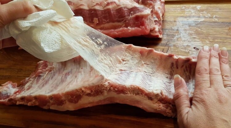 Close up of the membrane of pork ribs being removed by being pulled off gripped with paper towel