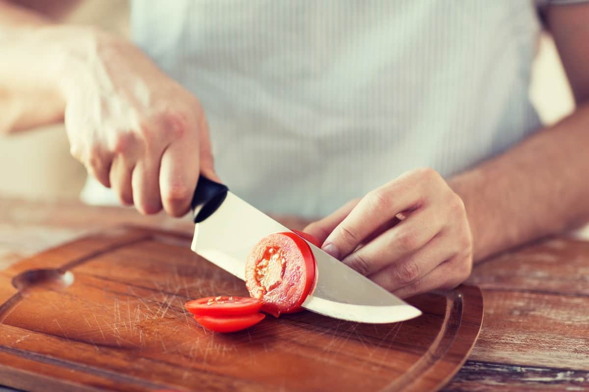 A male chef slicing a tomato with a sharp kn.