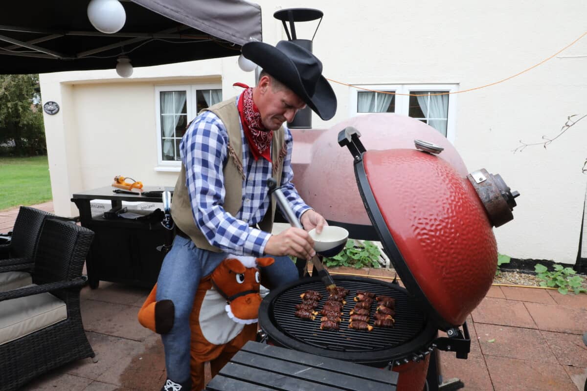 Mark Jenner dressed as a cowboy, brushing sauce onto food on a Kamado Joe Smoker.