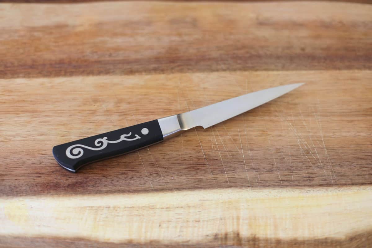 Top view of a paring knife on a wood chopping bo.