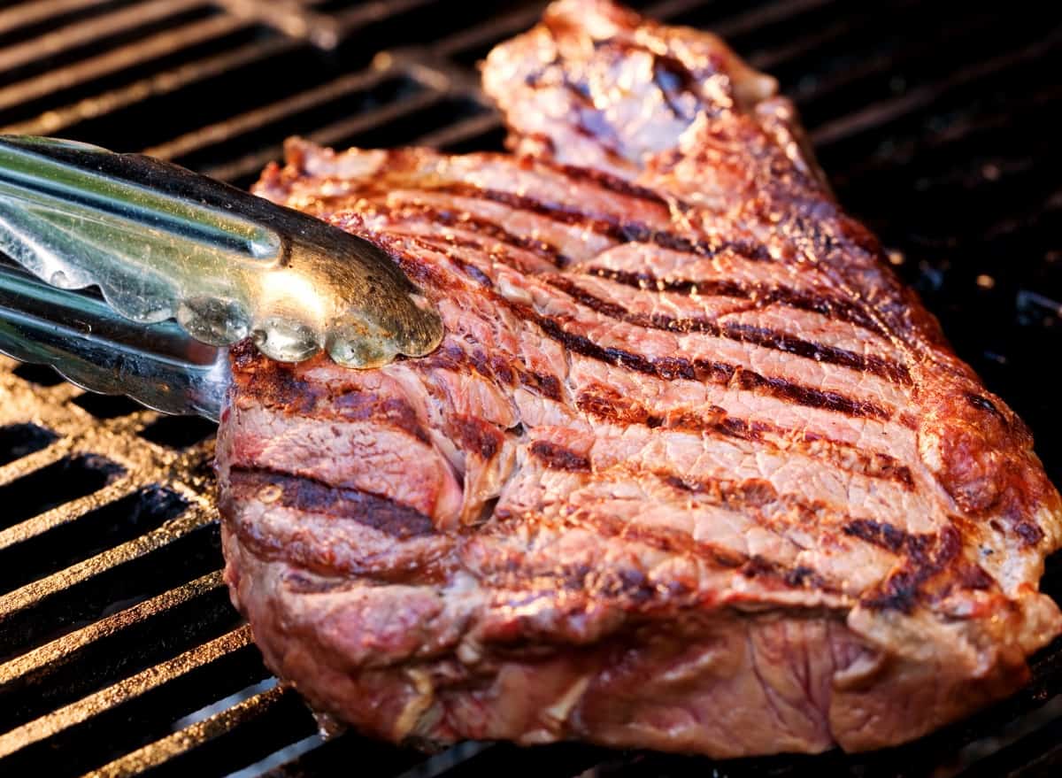 sirloin steak being turned over with tongs on a gr.