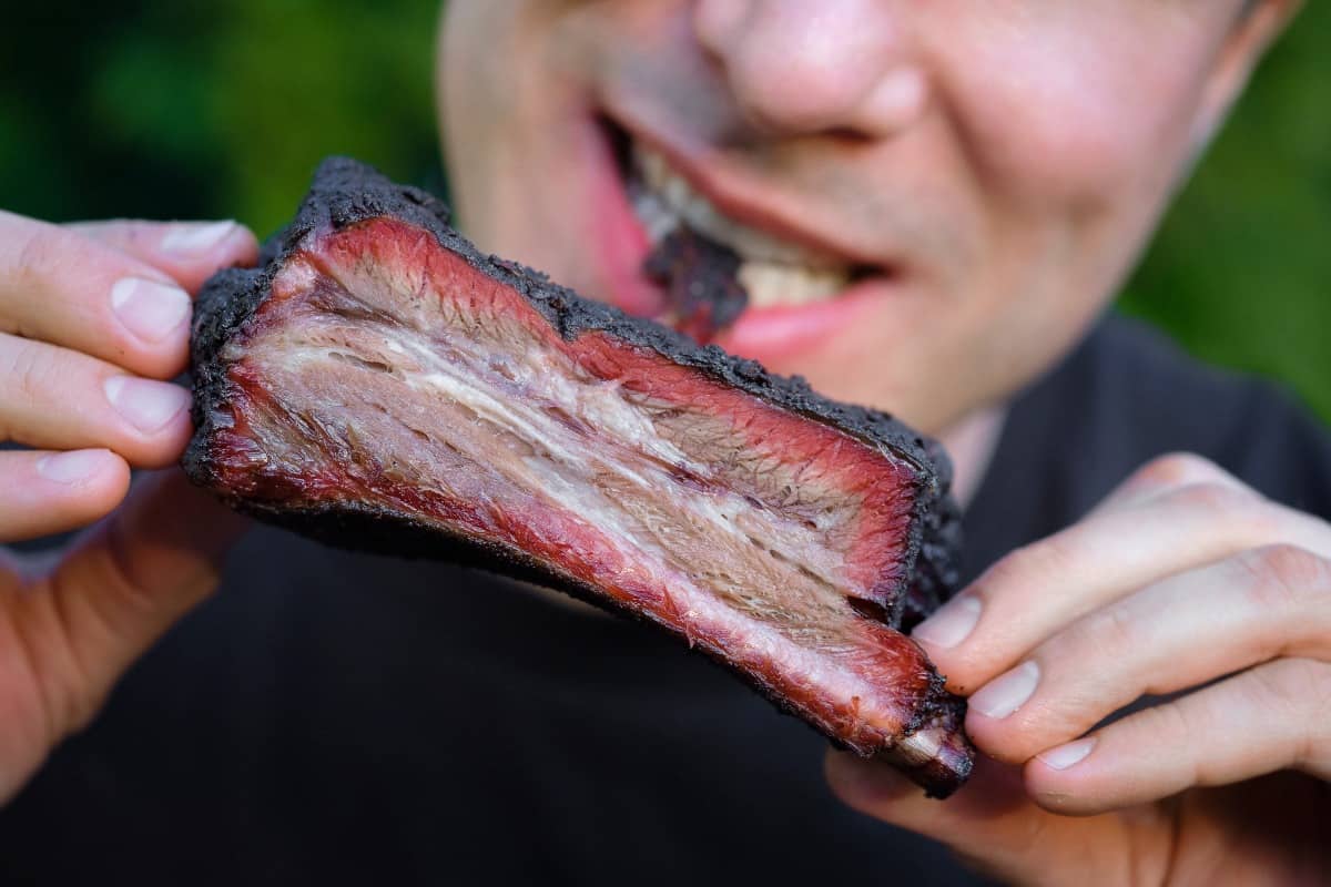 A person taking a bite out of a beef rib with a good smoke r.