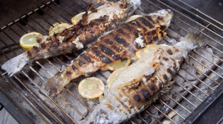 A hot grill with fish that seems to have stuck to the grate while being turned over