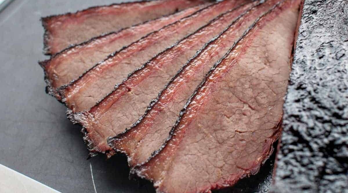The smoke ring seen in a few slices of smoked brisket fanned out on a chopping board.