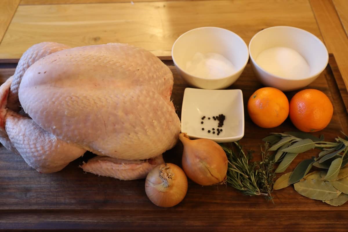 turkey and brine ingredients laid out on a cutting board, including onion, thyme, rosemary, oranges and salt.