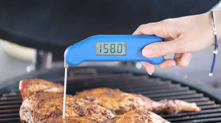 An instant read thermometer being used to take the temp of a spatchcock chicken on a grill