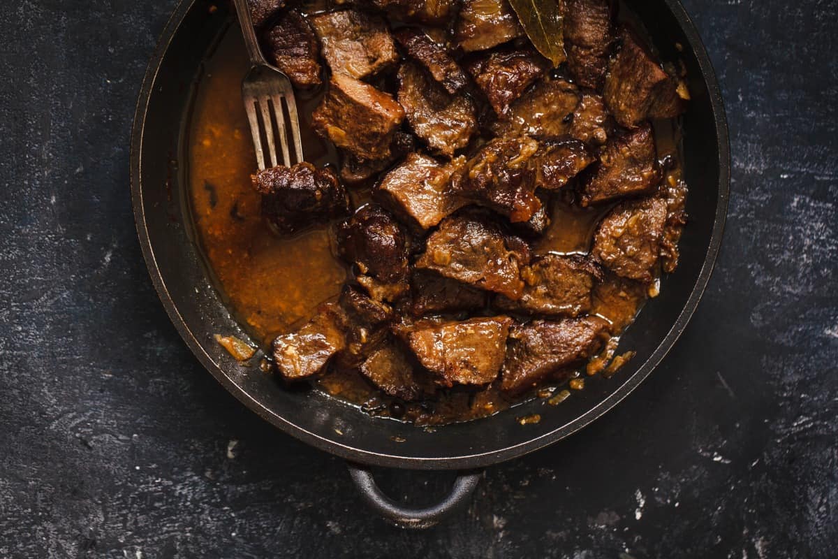 braised beef steak stew, overhead shot with a piece being lifted by a f.