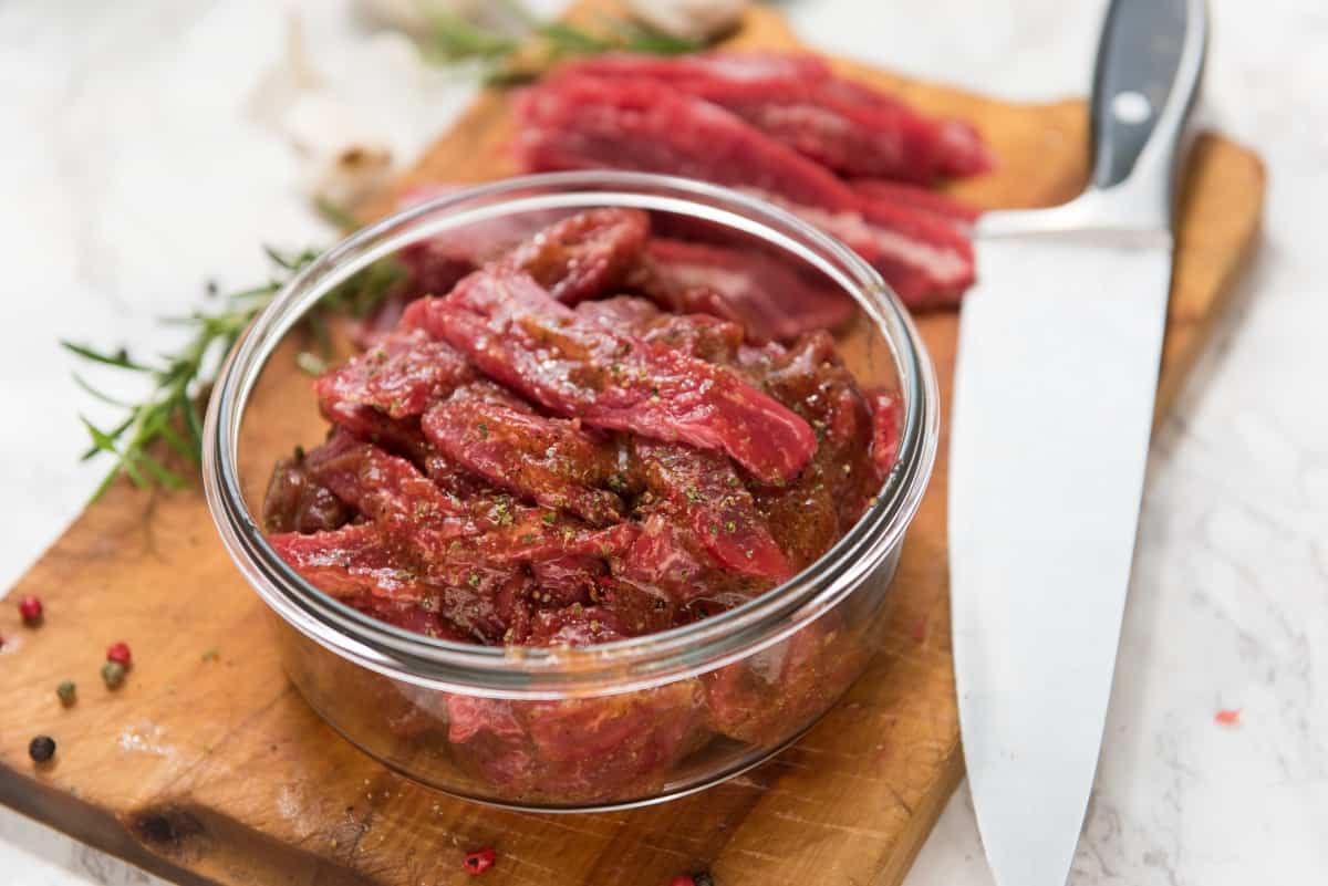 marinating flank steak in a bowl, on cutting board next to a large kn.