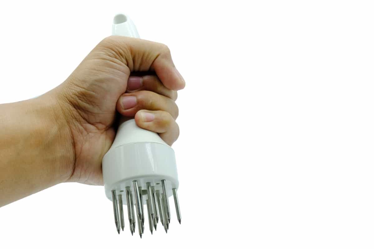 21 needle meat tenderizer in a mans left hand, isolated on wh.