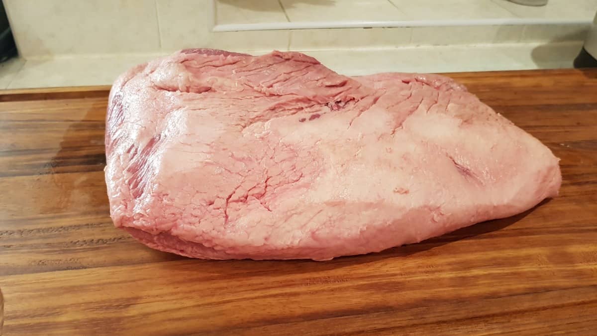 A whole packer brisket, fat side up, sitting on a cutting bo.