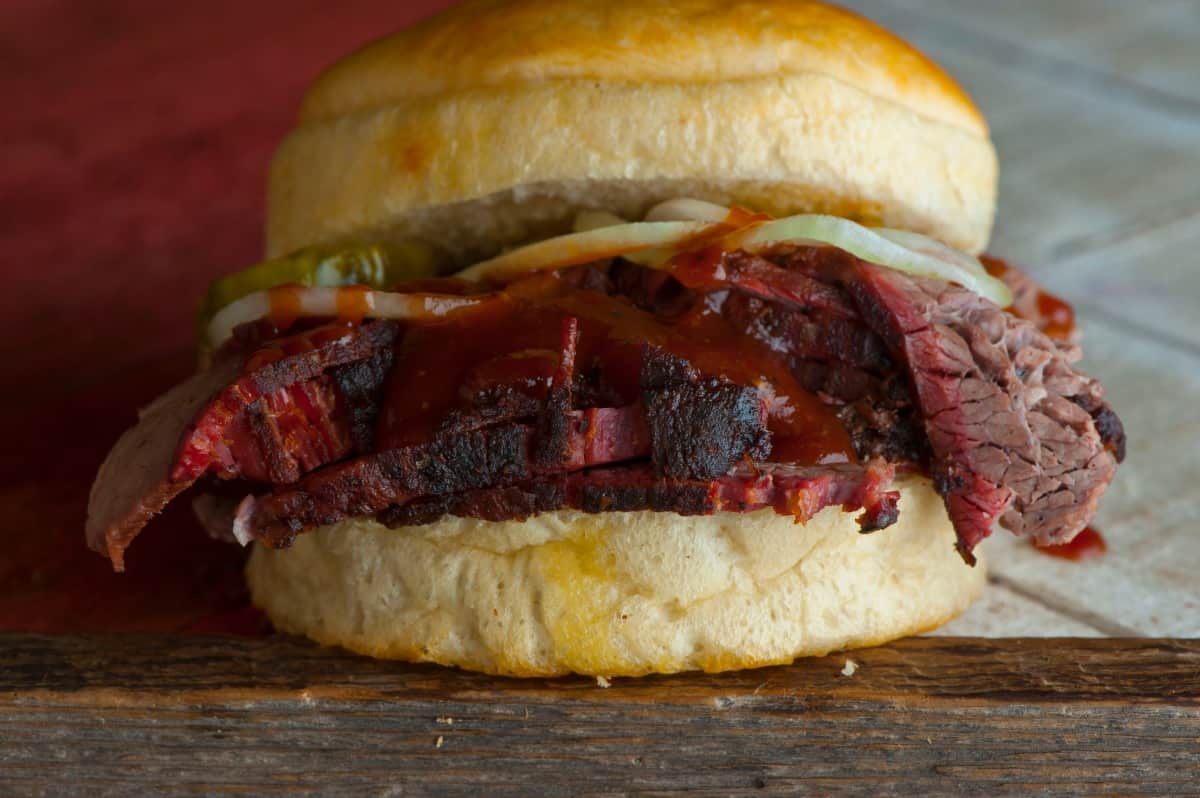 A brisket roll, with sauce and pickles on top of the sliced bris.