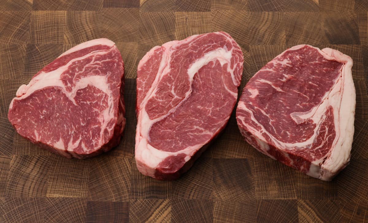 Three choice ribeye steaks on a wooden butchers block