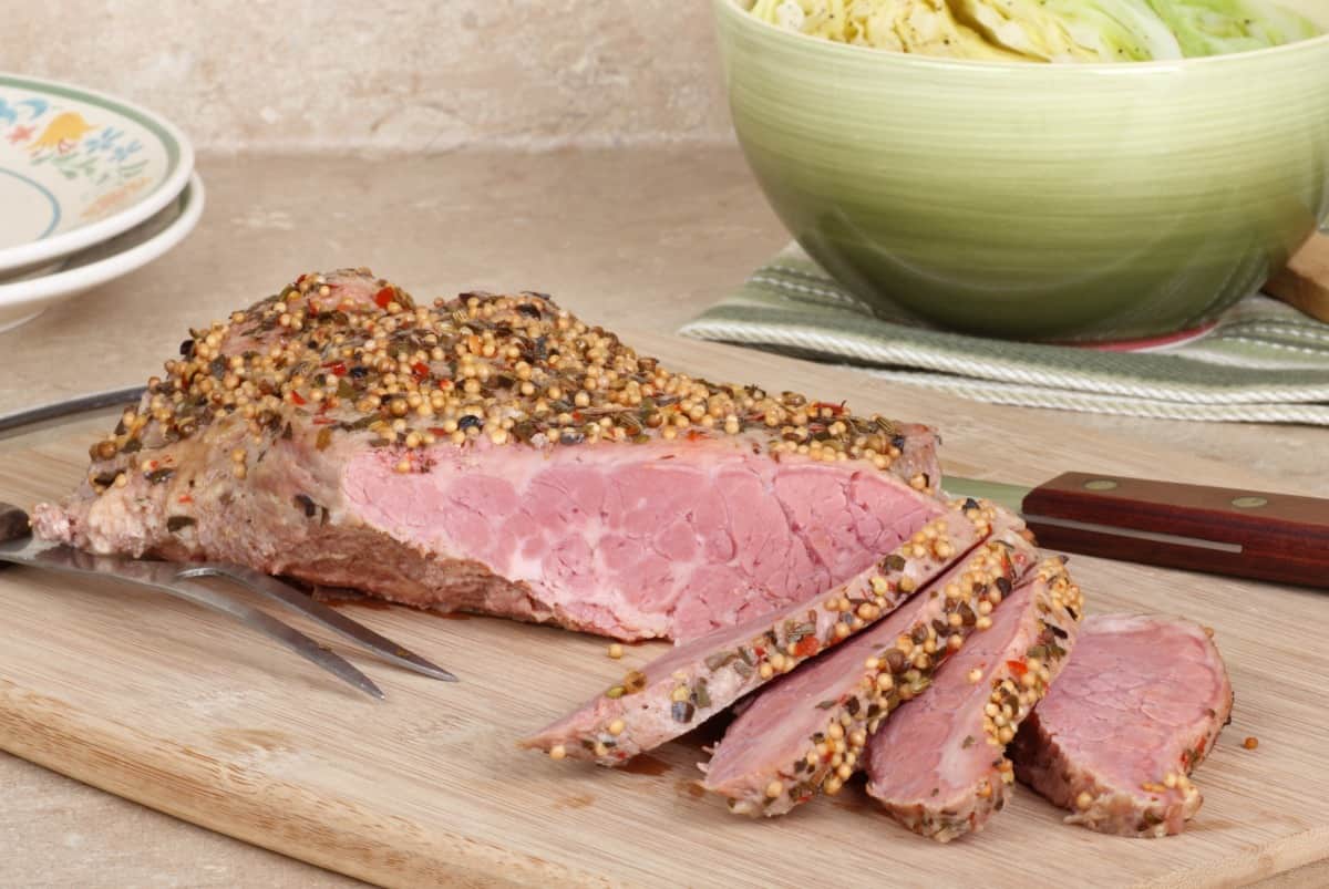 Sliced corned beef on a cutting board with a bowl of cabb.