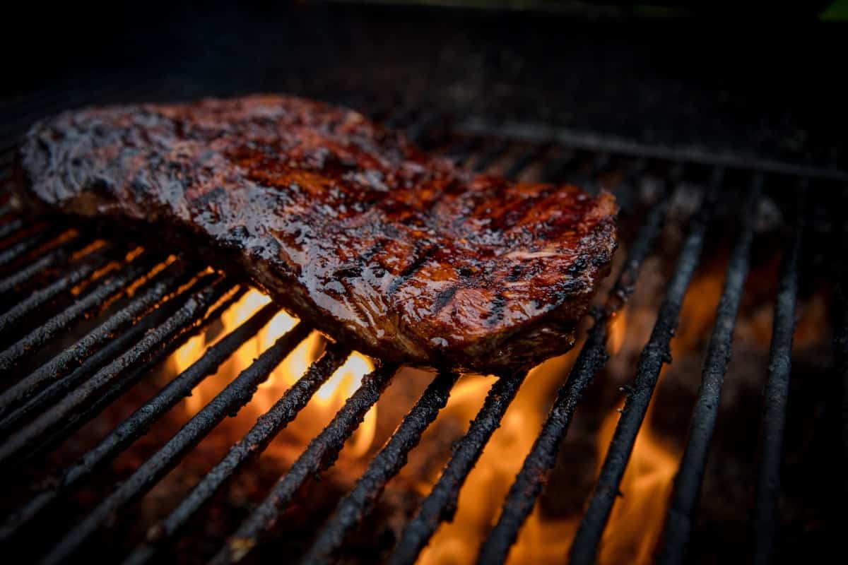 Flank steak being seared on a flaming gr.